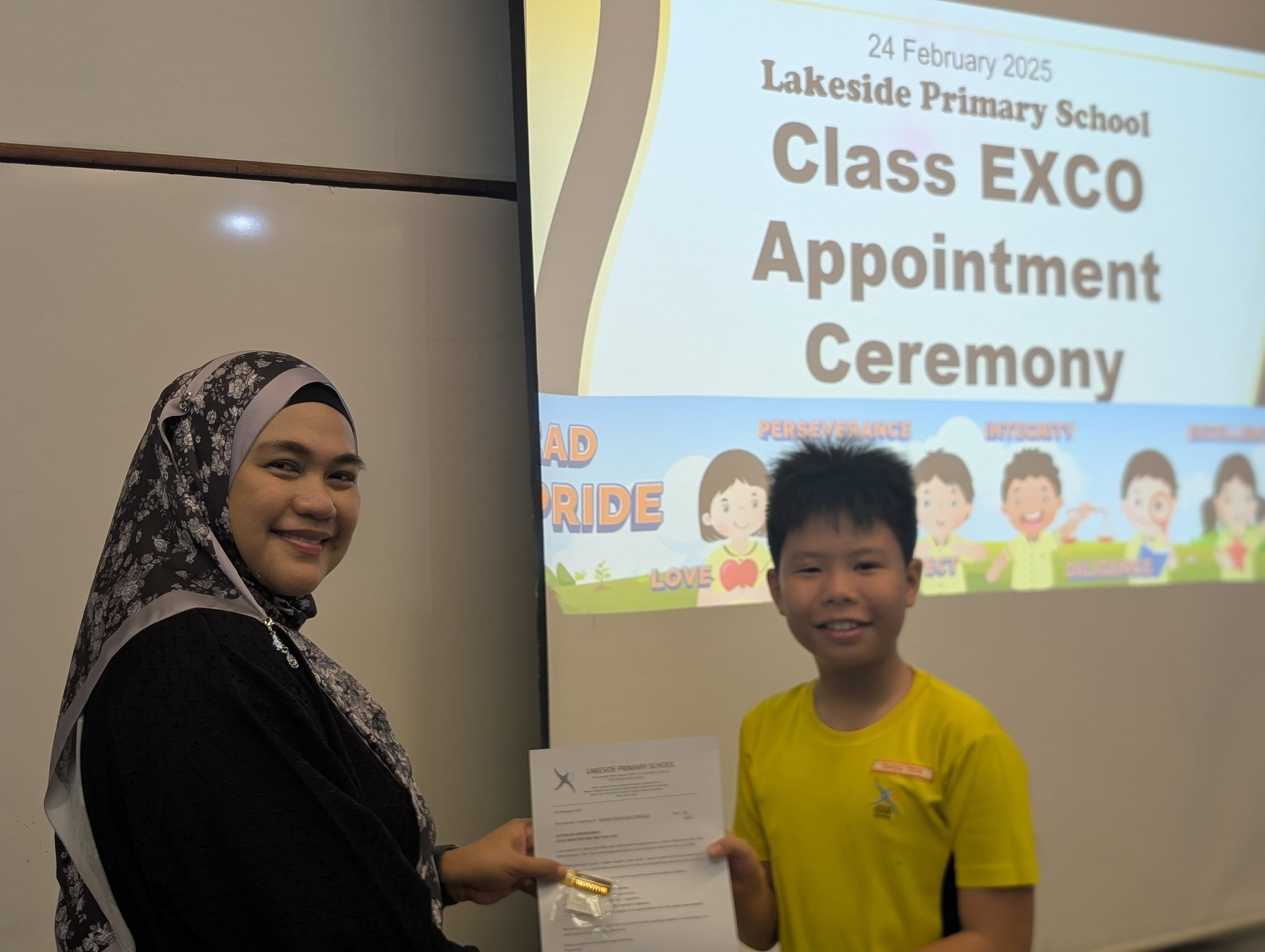 A teacher and student pose for a photo as the student receive their certificate of appointment
